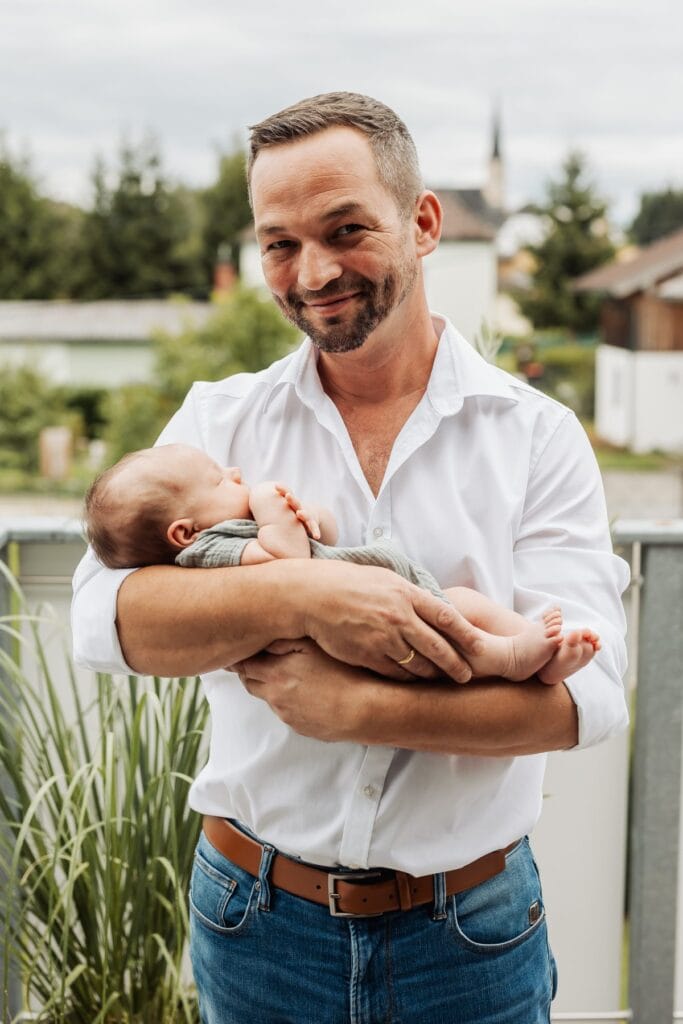 Ein Mann hält ein Baby vor einem Haus.