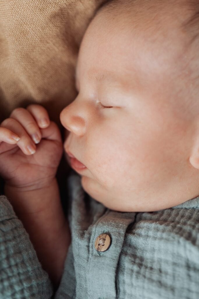 Ein Baby schläft auf einer Decke und hat die Hände auf dem Gesicht.