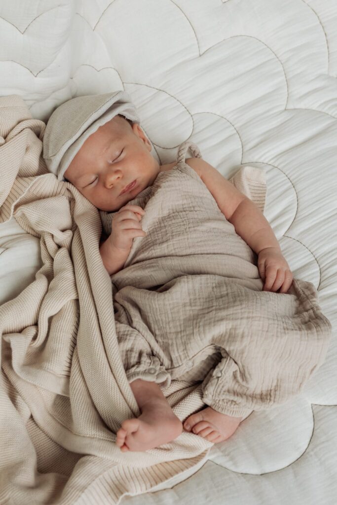 Ein Baby schläft auf einem Bett mit einer beigen Decke.