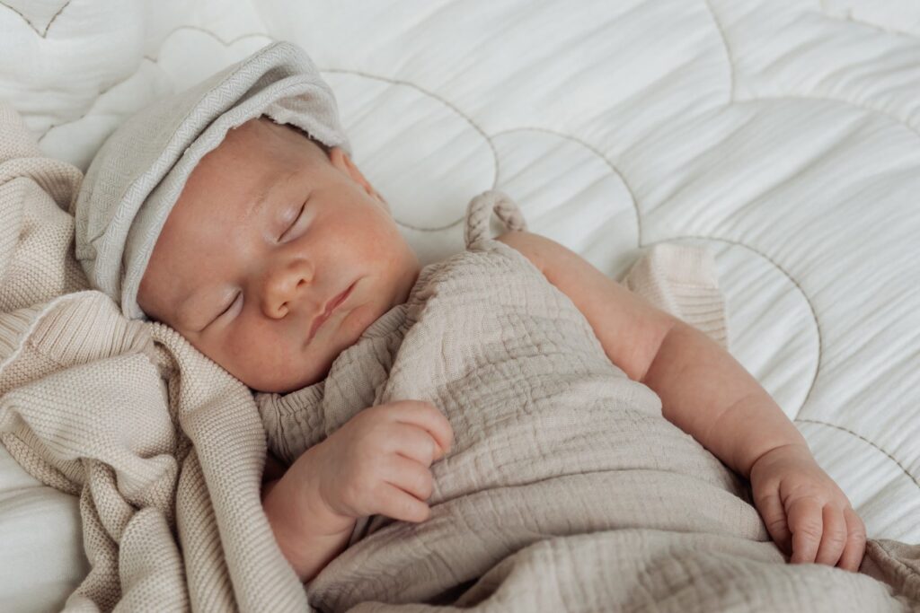 Ein Baby schläft auf einem Bett mit einer Mütze auf dem Kopf.