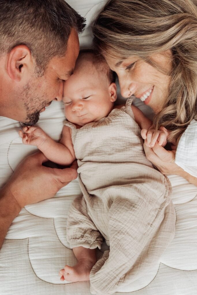 Ein Mann und eine Frau liegen mit einem Baby auf einem Bett.