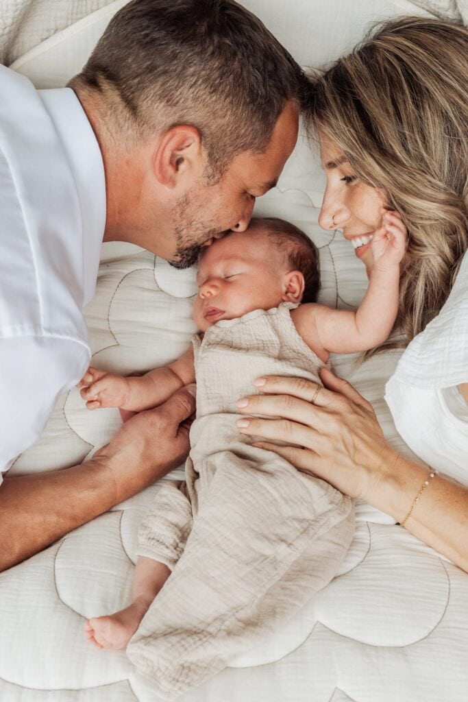Ein Mann und eine Frau liegen mit einem Baby im Arm auf einem Bett.