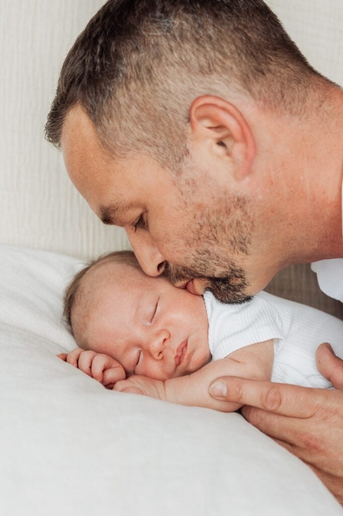 Ein Mann küsst sein Baby, während er auf einem Bett liegt.