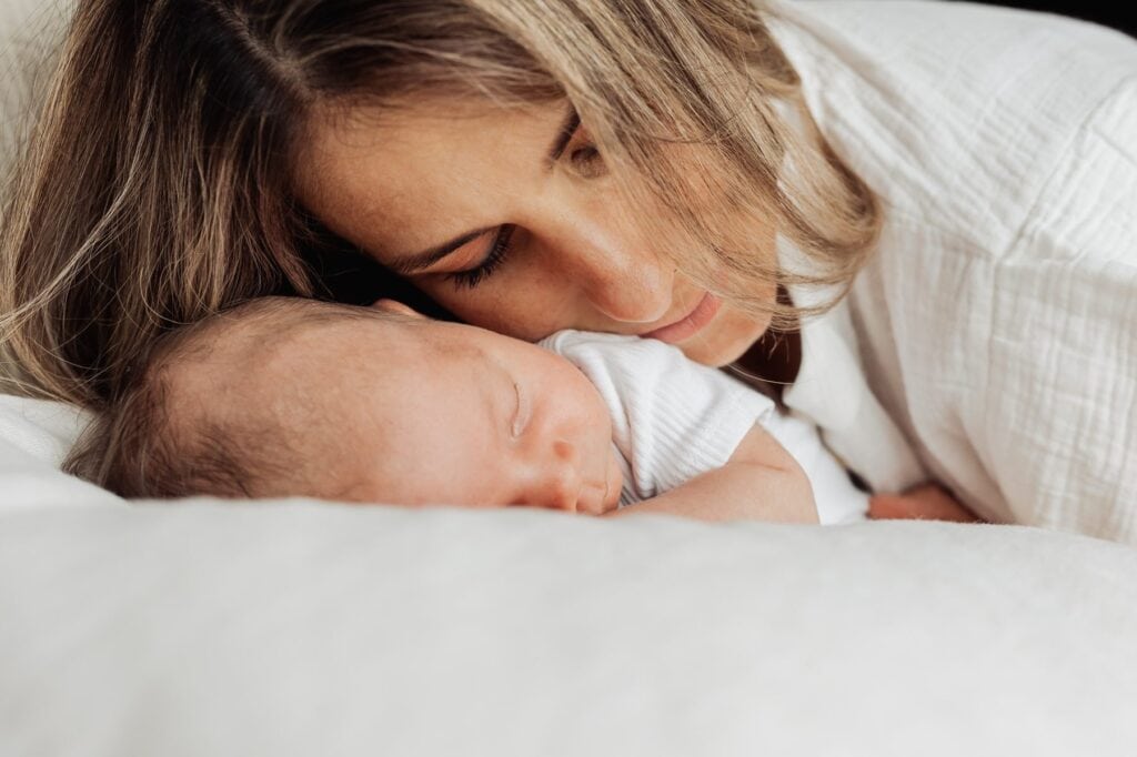 Eine Frau schläft mit ihrem Baby auf einem weißen Bett.