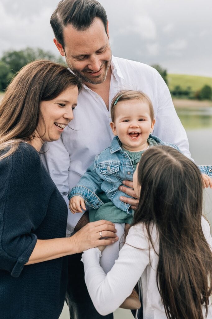 Ein Mann und eine Frau lächeln, als sie mit einem Baby in einer Jeansjacke und einem kleinen Mädchen mit langen Haaren draußen stehen.